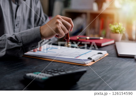 Financial approval and business agreement concept featuring a hand holding a seal stamp on a document. Ideal for management, accounting, and contracts. 126154590