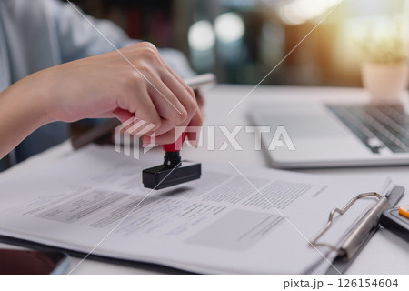 Close-up of hand using a red stamp on a legal document, indicating confirmation or validation in administrative work. 126154604