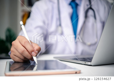 Close-up of a medical professional working on a tablet with a stylus, wearing a stethoscope, and using technology for patient care. 126154627