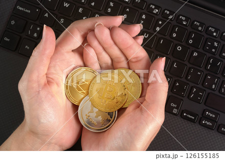 Woman holding golden coloured cryptocurrency coins in her hands over black laptop keyboard 126155185