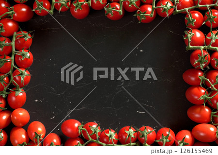 Red cherry tomatoes arranged in rectangular frame on black marble like board, view from above space for text in middle 126155469