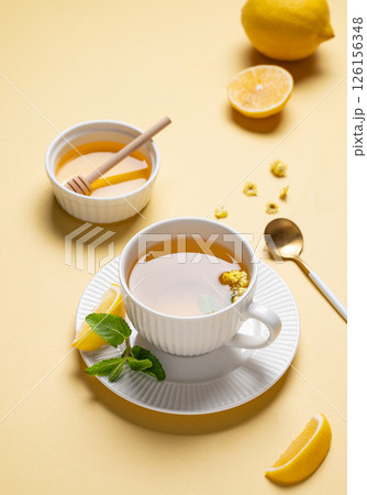 Cup of herbal tea with lemon, honey and mint on yellow background with citrus fruits and shadows. Cup of herbal tea with lemon, honey and mint on yellow background with citrus fruits and shadows. 126156348
