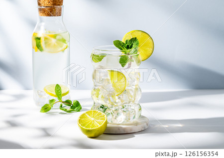 Mojito cocktail in a glass with lime, mint and ice on a white blue background with shadow and bottle Mojito cocktail in a glass with lime, mint and ice on a white blue background with shadow and bottle 126156354