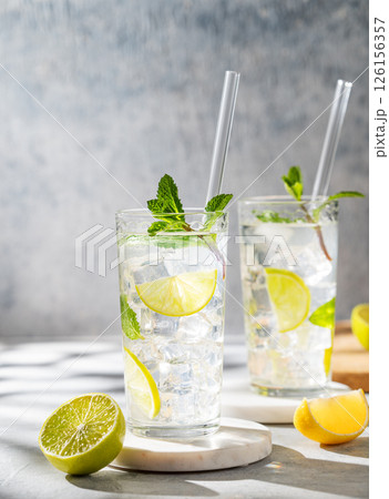 Two glasses mojito cocktail with fresh lime, mint and ice on light background with shadow. Two glasses mojito cocktail with fresh lime, mint and ice on light background with shadow. 126156357