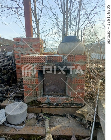 Weathered Red Brick Outdoor Oven in Rustic Rural Style with Rusty Metal Door and Earthenware Pot for Traditional Cooking 126156805