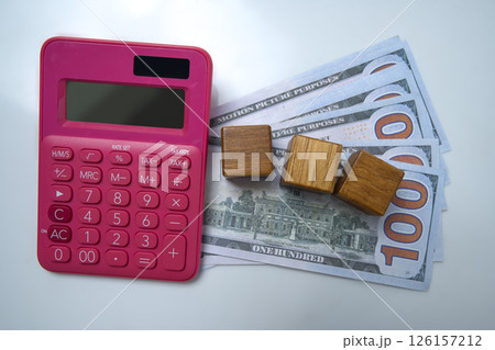 Top view of a pink calculator and a pile of 100 dollar banknotes with wooden cubes on a white background. Mockup or Copy space. Concept of wealth, saving or investment, and tax 126157212