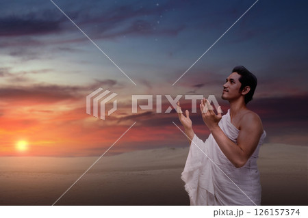Indonesian southeast asian muslim man wearing white traditional clothes or ihram raises his hand and prays on the hajj. Concept of hajj or umrah 126157374
