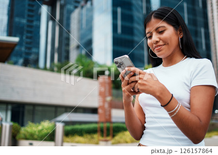 A young woman is using her smartphone while enjoying the urban city setting around her 126157864