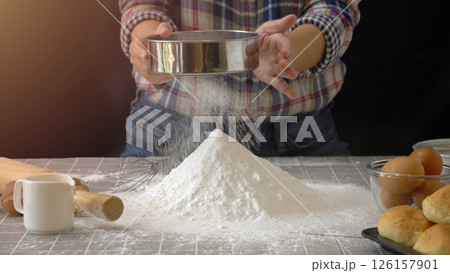 Artisan bread dough preparation. Use sieve or colander to sift flour into pile of flour for handmade bread with bakery equipment tool, black background. professional baker process at work. Artisan bread dough preparation. Use sieve or colander to sift flour into pile of flour for handmade bread with bakery equipment tool, black background. professional baker process at work. 126157901