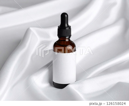 photograph of a dark amber oil bottle resting elegantly on a pristine white silk 126158024