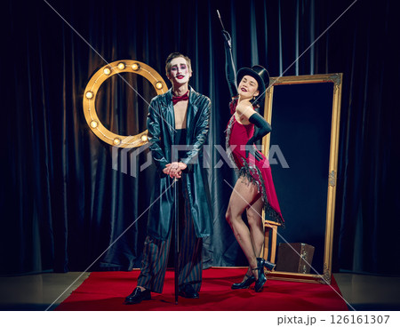 Stylized cabaret couple poses under lights wearing theatrical clothes cane hat and dramatic expressions. 126161307
