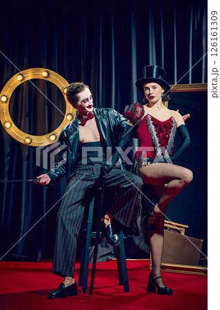 Male and female cabaret performer, dressed in striking vintage attire including top hat and sparkly red dress, pose dynamically on red carpet 126161309