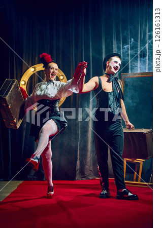 Joyful cabaret couple walks forward holding hands smiling in red gloves and hat with suitcases. Joyful cabaret couple walks forward holding hands smiling in red gloves and hat with suitcases. 126161313