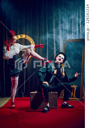 Cabaret woman raising leg toward seated man in dramatic pose with red gloves corset suitcase smoky lights Cabaret woman raising leg toward seated man in dramatic pose with red gloves corset suitcase smoky lights 126161314