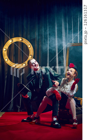 Laughing cabaret performers, man and woman pose in vintage costumes on red carpet with dramatic expressions. 126161317