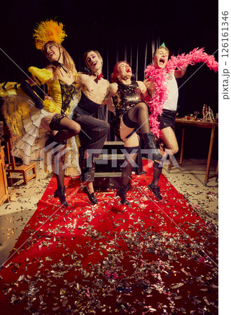 Four energetic cabaret performers posing on red carpet covered in confetti, joyful, theatrical expressions in their vintage attire. Four energetic cabaret performers posing on red carpet covered in confetti, joyful, theatrical expressions in their vintage attire. 126161346