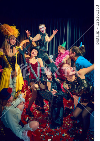 Cabaret performers pose in vintage costumes on red carpet with dramatic expressions and stage props. 126161353