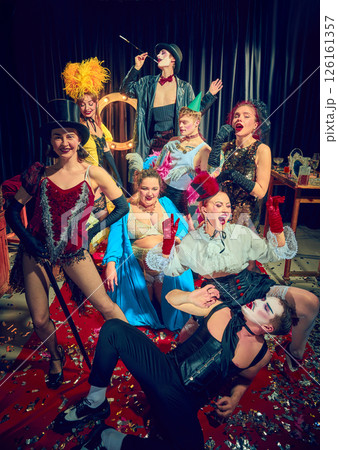 Cabaret performers pose in vintage costumes on red carpet with dramatic expressions and stage props. 126161357