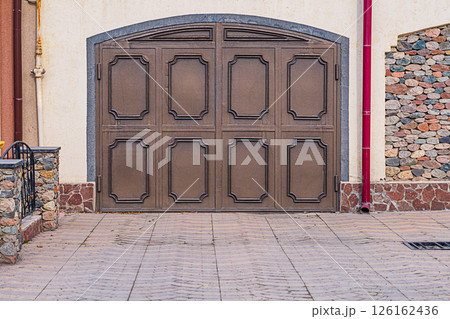 Parking space in front of the entrance group of the garage of a private house with metal swing gates. Residential area of the city with one-story residential premises Parking space in front of the entrance group of the garage of a private house with metal swing gates. Residential area of the city with one-story residential premises 126162436