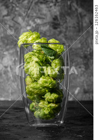 Transparent glass filled with hops on the table. Dark background with place for text. Ingredient for beer. Transparent glass filled with hops on the table. Dark background with place for text. Ingredient for beer. 126162463