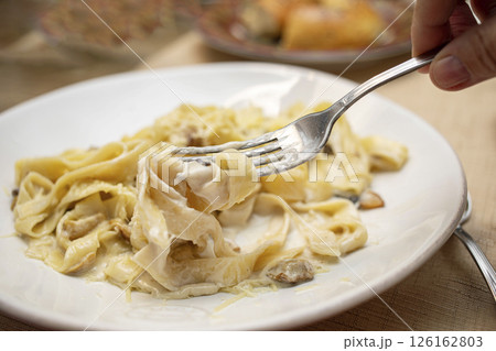 Creamy fettuccine pasta dish served on a white plate with fork lifting noodles for a delicious meal Creamy fettuccine pasta dish served on a white plate with fork lifting noodles for a delicious meal 126162803