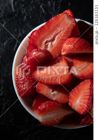 Red ripe strawberries in a saucer on a black background close-up. 126163131