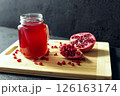 Glass of pomegranate juice and cutted pomegranate with seeds lie on a wooden cutting board on the concrete background 126163174