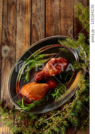 Smoked chicken drumsticks and juniper branches on a wooden table. 126164230