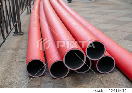 Red pre-insulated pipes laying on the sidewalk during city construction works 126164594