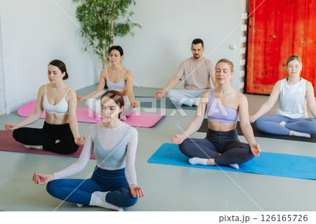 Yoga mindfulness meditation. Group of sporty people doing exercise in studio for class for yoga wellness mindfulness meditation. Men women practicing yoga sitting in lotus pose meditating relaxing 126165726
