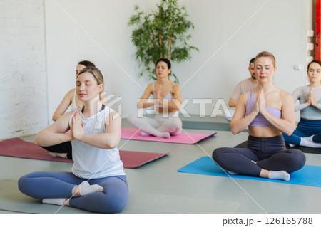 Yoga mindfulness meditation. Group of sporty people doing exercise in studio for class for yoga wellness mindfulness meditation. Men women practicing yoga sitting in lotus pose meditating relaxing Yoga mindfulness meditation. Group of sporty people doing exercise in studio for class for yoga wellness mindfulness meditation. Men women practicing yoga sitting in lotus pose meditating relaxing 126165788