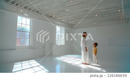 Mother and child interacting in a bright, minimalistic white room during daytime 126166639