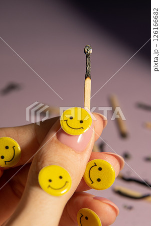A burnt match in a hand among many matches on a light purple background. Yellow emoticons, creative. 126166682