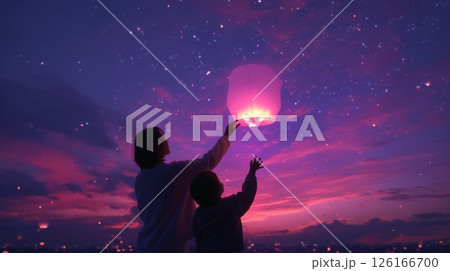Releasing floating lanterns into a vibrant twilight sky at a serene outdoor location with a child 126166700