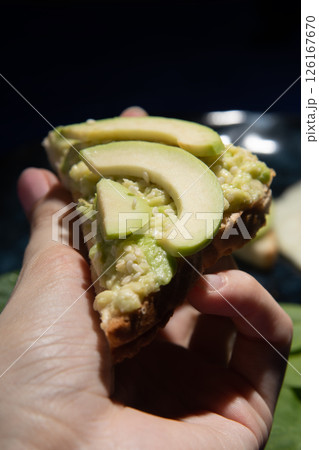 Sandwich with avocado in hand on a dark background close-up. Sandwich with avocado in hand on a dark background close-up. 126167670