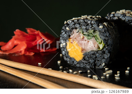 Black rice. Rolls with cheese, ham, and cucumber. Sticks and ginger are licked near the land. 126167989