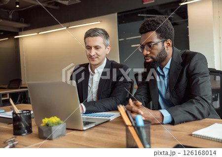 Two businessmen sitting in the office at the laptop and working on the project Two businessmen sitting in the office at the laptop and working on the project 126168014