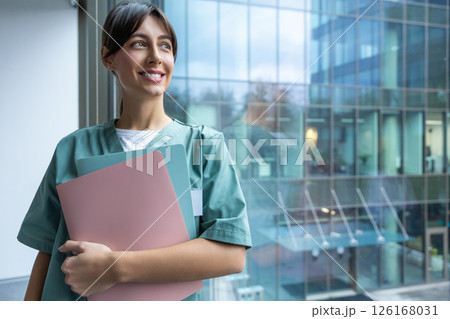 Smiling dark-haired female doctor in lab coat with a medical history in hands 126168031
