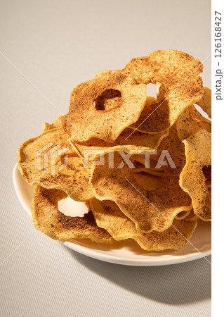 Dehydrated apple slices with powdered cinnamon on a plate. Close-up studio photo. 126168427