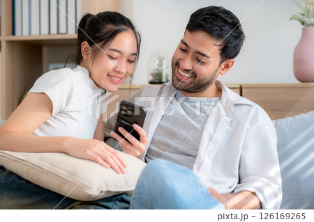 Young asian couple relax sitting on sofa looking smartphone together in living room. 126169265