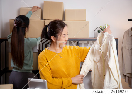 Two young asian woman live online clothing store while showing clothing with tablet on social. Two young asian woman live online clothing store while showing clothing with tablet on social. 126169275