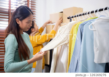Two young asian woman arranging clothes in store for preparation delivery, seller choice clothes. Two young asian woman arranging clothes in store for preparation delivery, seller choice clothes. 126169276