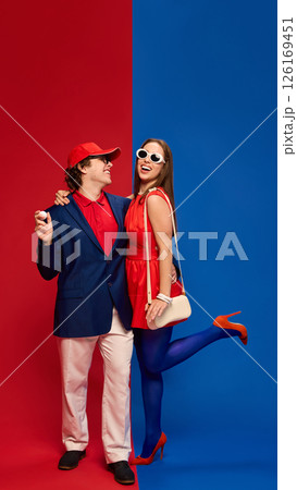 Cheerful young man and woman, couple in golf-inspired outfits, smiling and embracing against vivid red and blue background. Cheerful young man and woman, couple in golf-inspired outfits, smiling and embracing against vivid red and blue background. 126169451