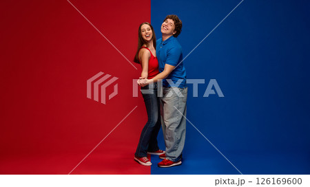 Happy couple, man and woman laughing, hugging in dynamic pose on red blue background, showing joy, love and connection. Happy couple, man and woman laughing, hugging in dynamic pose on red blue background, showing joy, love and connection. 126169600
