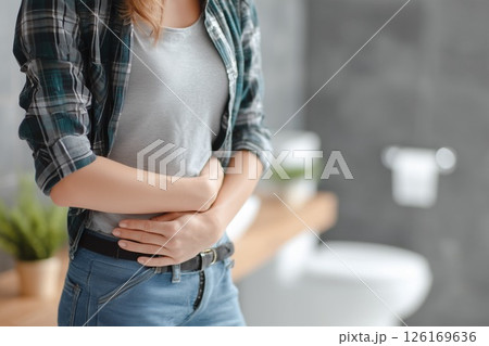 トイレで手でお腹を押さえる若い女性。腹痛や胃痛、ストレスを表す体調不良のイメージ 126169636
