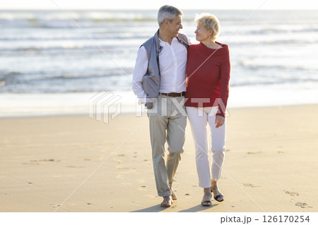 Happy senior couple walking on the beach at sunset 126170254