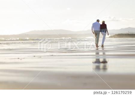 Senior couple walking on the beach at sunset, enjoying retirement travel 126170259