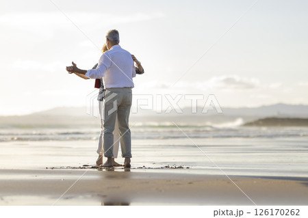 Senior couple dancing barefoot on the beach at sunset 126170262