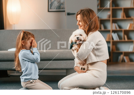 Woman is giving pet for the girl. Present for the daughter. Mother is at home with maltese dog Woman is giving pet for the girl. Present for the daughter. Mother is at home with maltese dog 126170896