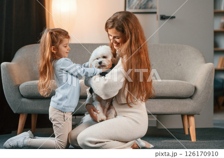 Sitting on the floor. Mother with daughter is at home with maltese dog Sitting on the floor. Mother with daughter is at home with maltese dog 126170910
